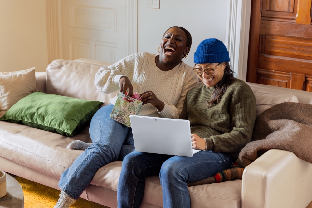 Two women on a couch in their home, laughing