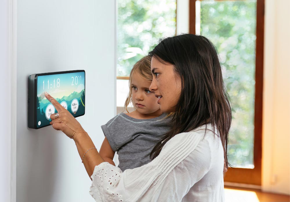 A mother holding her daughter in her arms to show her the NeHo tablet mounted on their wall and explaining her how to read their energy consumption and why it matters to save energy